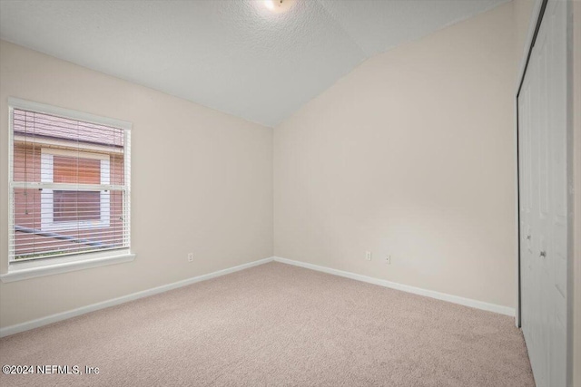 carpeted spare room featuring a textured ceiling and lofted ceiling