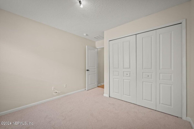 unfurnished bedroom with light carpet, a textured ceiling, and a closet