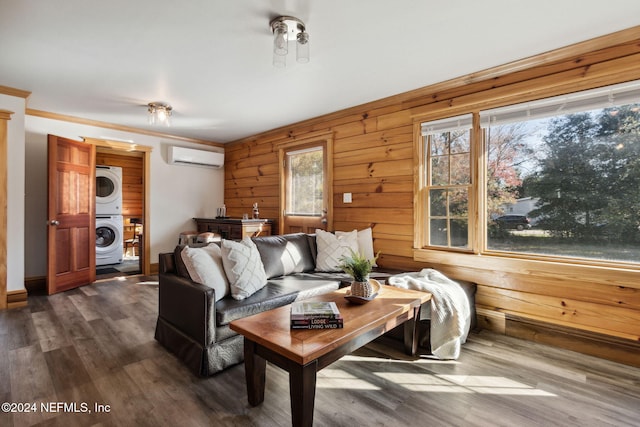 living room featuring a healthy amount of sunlight, hardwood / wood-style floors, stacked washing maching and dryer, and a wall mounted air conditioner