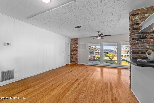 unfurnished living room featuring ceiling fan, light hardwood / wood-style floors, and brick wall