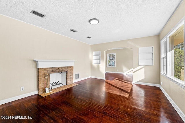 unfurnished living room featuring hardwood / wood-style floors, a textured ceiling, and a brick fireplace