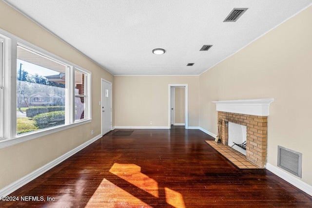 unfurnished living room with a textured ceiling, a wealth of natural light, dark hardwood / wood-style floors, and a brick fireplace