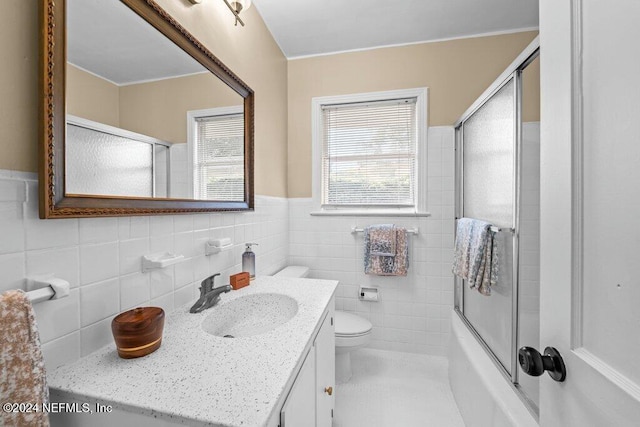 full bathroom with vanity, toilet, bath / shower combo with glass door, and tile walls