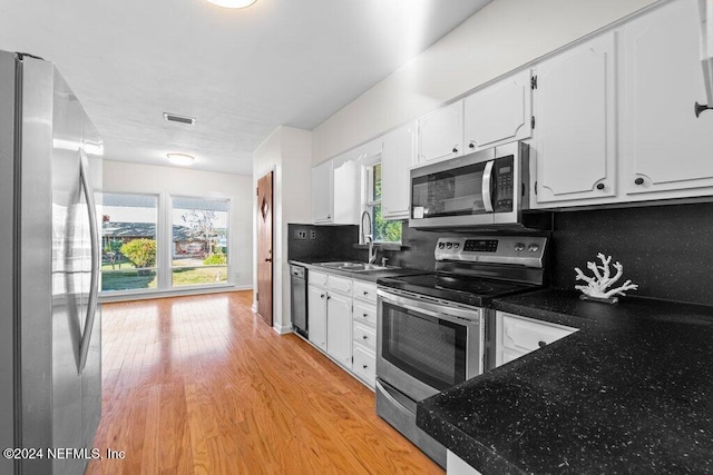 kitchen with backsplash, stainless steel appliances, sink, white cabinets, and light hardwood / wood-style floors