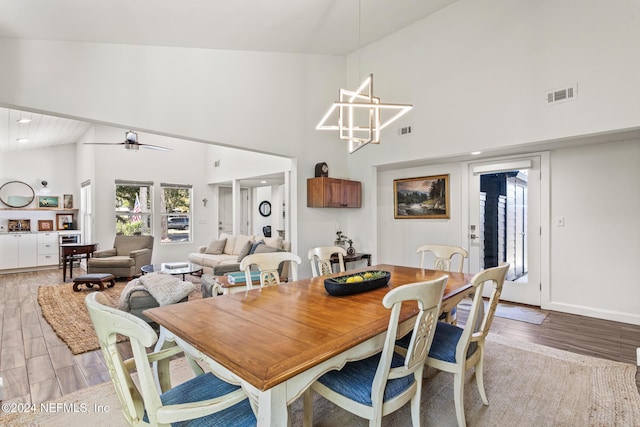 dining space featuring ceiling fan with notable chandelier, light hardwood / wood-style floors, and high vaulted ceiling