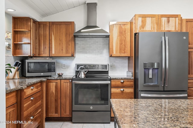 kitchen featuring stainless steel appliances, vaulted ceiling, wall chimney range hood, light tile patterned floors, and dark stone countertops