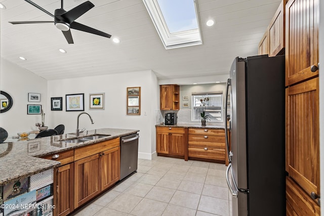 kitchen featuring stainless steel appliances, light stone counters, a skylight, and sink