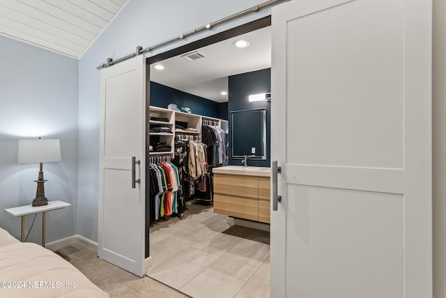 walk in closet with light tile patterned floors, a barn door, lofted ceiling, and sink