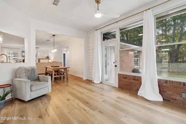 living area with ceiling fan, ornamental molding, brick wall, and light wood-type flooring