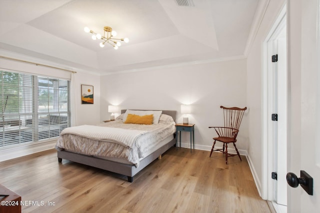 bedroom with a raised ceiling, an inviting chandelier, light hardwood / wood-style floors, and ornamental molding