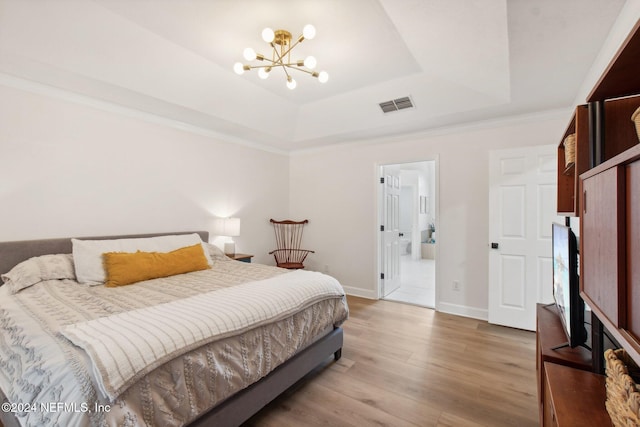 bedroom featuring hardwood / wood-style floors, crown molding, connected bathroom, a tray ceiling, and a notable chandelier