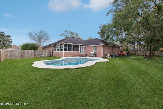 back of property featuring a sunroom, a fenced in pool, and a lawn