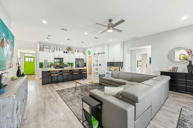 living room featuring recessed lighting, visible vents, light wood-style flooring, and a barn door