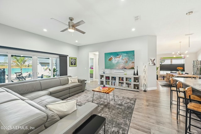 living room featuring recessed lighting, visible vents, light wood-type flooring, baseboards, and ceiling fan with notable chandelier