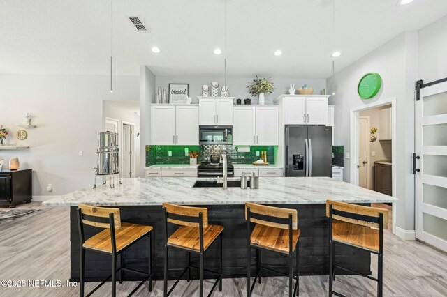 kitchen featuring a barn door, stainless steel appliances, a sink, white cabinets, and tasteful backsplash