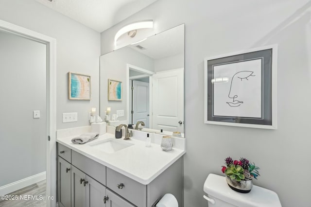 half bathroom featuring wood finished floors, vanity, toilet, and baseboards