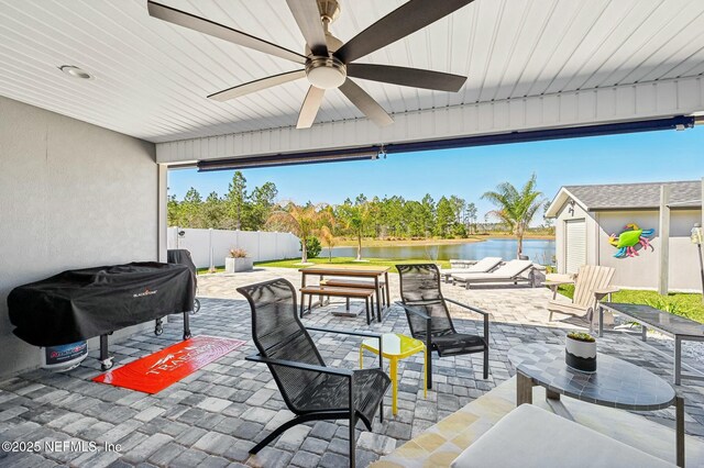 view of patio with a water view, ceiling fan, fence, and grilling area