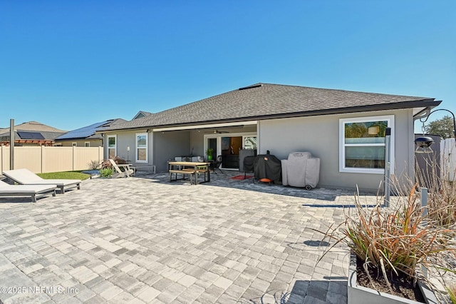 rear view of property featuring a shingled roof, fence, a patio area, an outdoor living space, and stucco siding