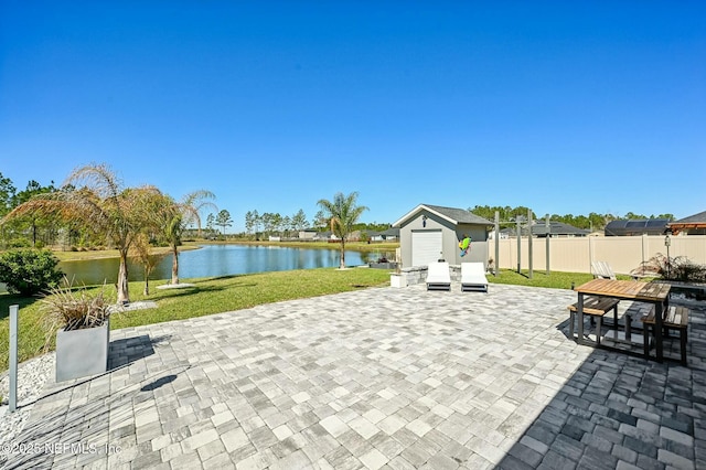 view of patio with an outbuilding, a water view, fence, and a storage unit