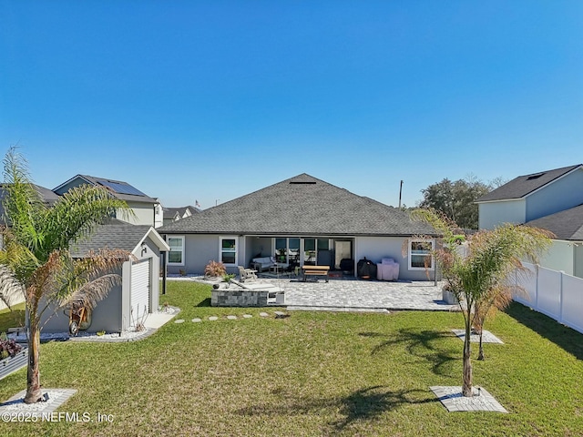 rear view of house with an outdoor structure, fence, a yard, roof with shingles, and a patio area