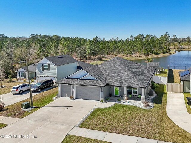 traditional-style house with driveway, an attached garage, a water view, fence, and a front yard