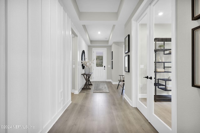 corridor featuring french doors, light hardwood / wood-style floors, and a tray ceiling