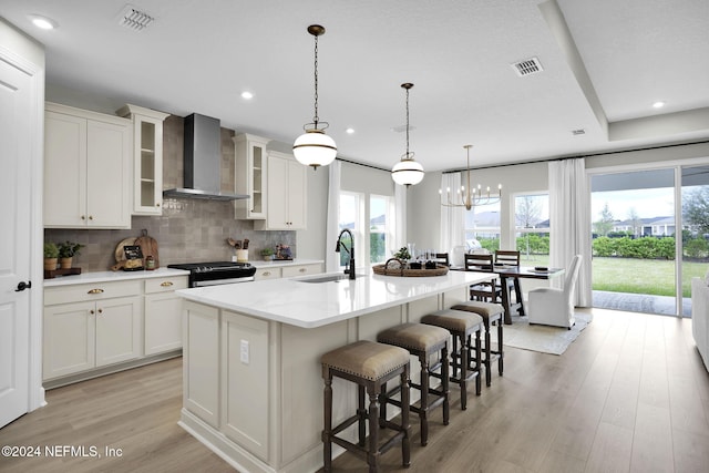 kitchen with a wealth of natural light, sink, wall chimney exhaust hood, and an island with sink