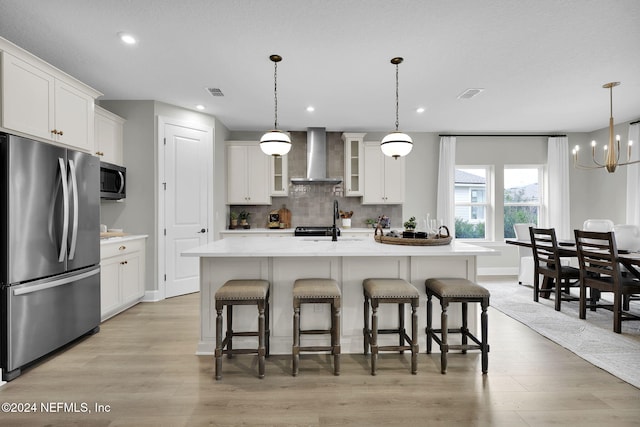 kitchen featuring appliances with stainless steel finishes, a center island with sink, white cabinetry, and wall chimney range hood