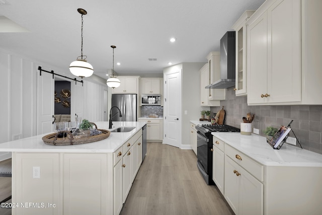 kitchen featuring pendant lighting, wall chimney exhaust hood, a barn door, an island with sink, and stainless steel appliances