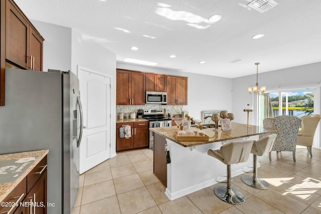 kitchen featuring an island with sink, stainless steel appliances, decorative light fixtures, light stone countertops, and sink