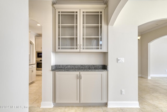 bar with appliances with stainless steel finishes, dark stone counters, light tile patterned floors, and ornamental molding