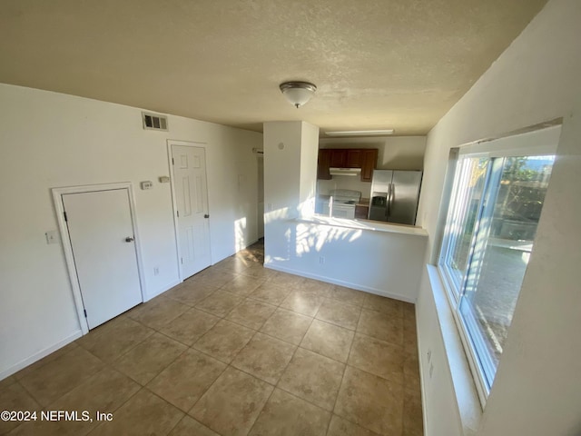 kitchen with kitchen peninsula, stainless steel fridge with ice dispenser, light tile patterned flooring, and electric stove