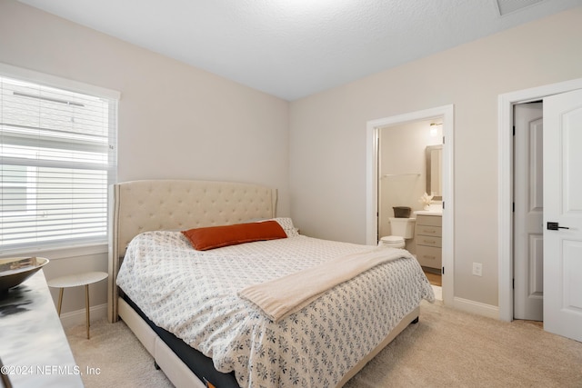 bedroom featuring a textured ceiling, ensuite bathroom, and light colored carpet