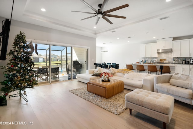 living room featuring a tray ceiling, ceiling fan, and light hardwood / wood-style flooring