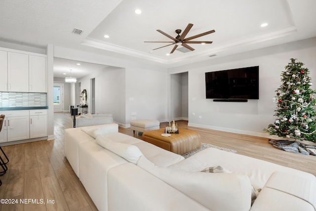 living room featuring a tray ceiling, ceiling fan, and light hardwood / wood-style floors