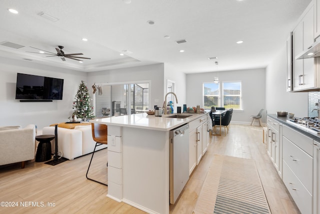 kitchen with white cabinets, sink, light hardwood / wood-style flooring, stainless steel dishwasher, and an island with sink