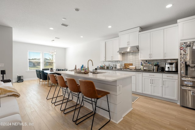 kitchen featuring a kitchen island with sink, sink, light hardwood / wood-style flooring, stainless steel fridge, and white cabinetry