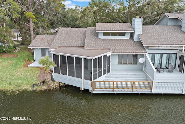 back of house with a sunroom, a deck with water view, and a lawn