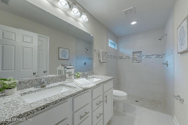 bathroom with vanity, a tile shower, a textured ceiling, and toilet