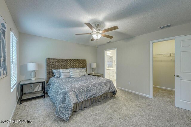 carpeted bedroom featuring ensuite bathroom, a walk in closet, ceiling fan, a textured ceiling, and a closet