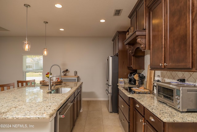 kitchen featuring appliances with stainless steel finishes, backsplash, light stone counters, a kitchen island with sink, and sink