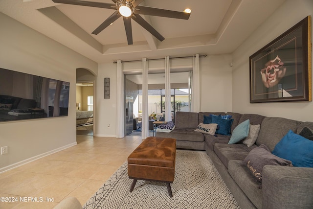 living room with light tile patterned floors, a raised ceiling, and ceiling fan