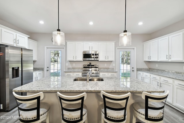 kitchen featuring a kitchen island with sink, sink, hanging light fixtures, and appliances with stainless steel finishes