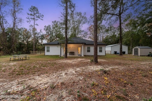 back house at dusk featuring a patio and a storage shed