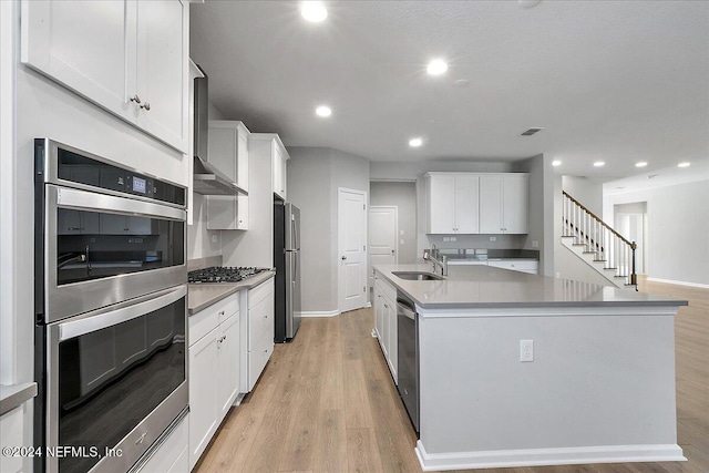 kitchen with a kitchen island with sink, sink, light wood-type flooring, white cabinetry, and stainless steel appliances