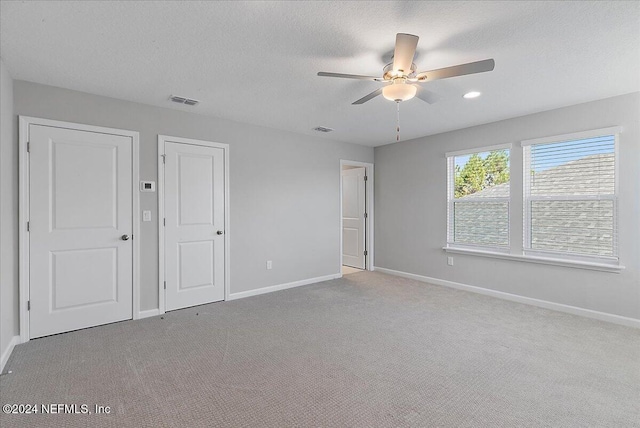 unfurnished bedroom featuring a textured ceiling, light colored carpet, and ceiling fan