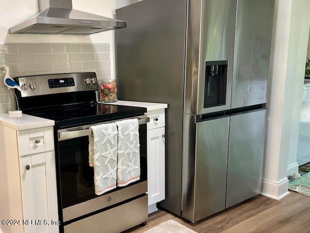 kitchen with wall chimney exhaust hood, tasteful backsplash, stainless steel appliances, light hardwood / wood-style floors, and white cabinets