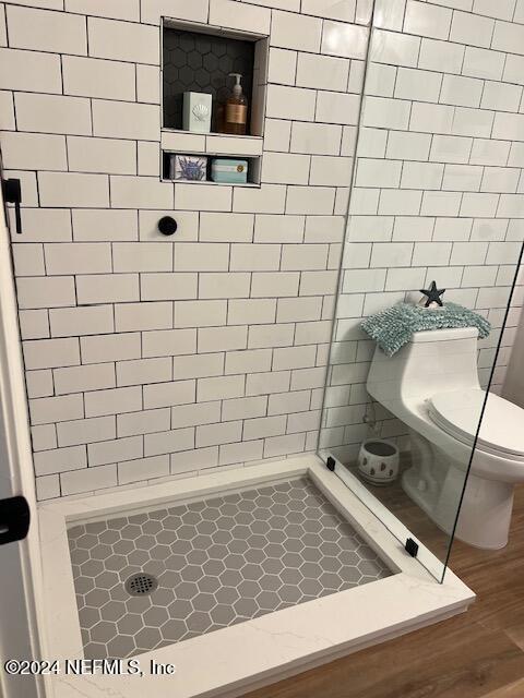 bathroom featuring toilet, hardwood / wood-style floors, and a tile shower