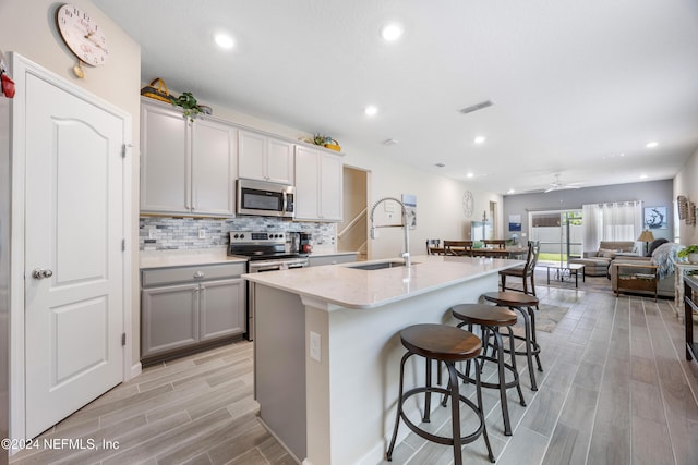 kitchen featuring a center island with sink, sink, ceiling fan, gray cabinets, and stainless steel appliances