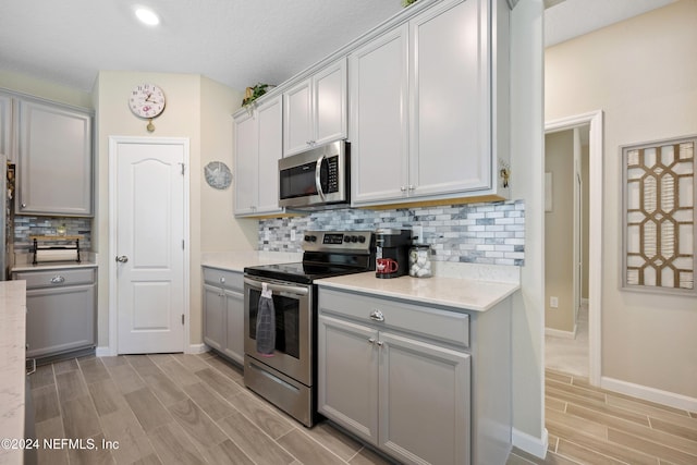 kitchen featuring decorative backsplash, gray cabinets, light wood-type flooring, and appliances with stainless steel finishes